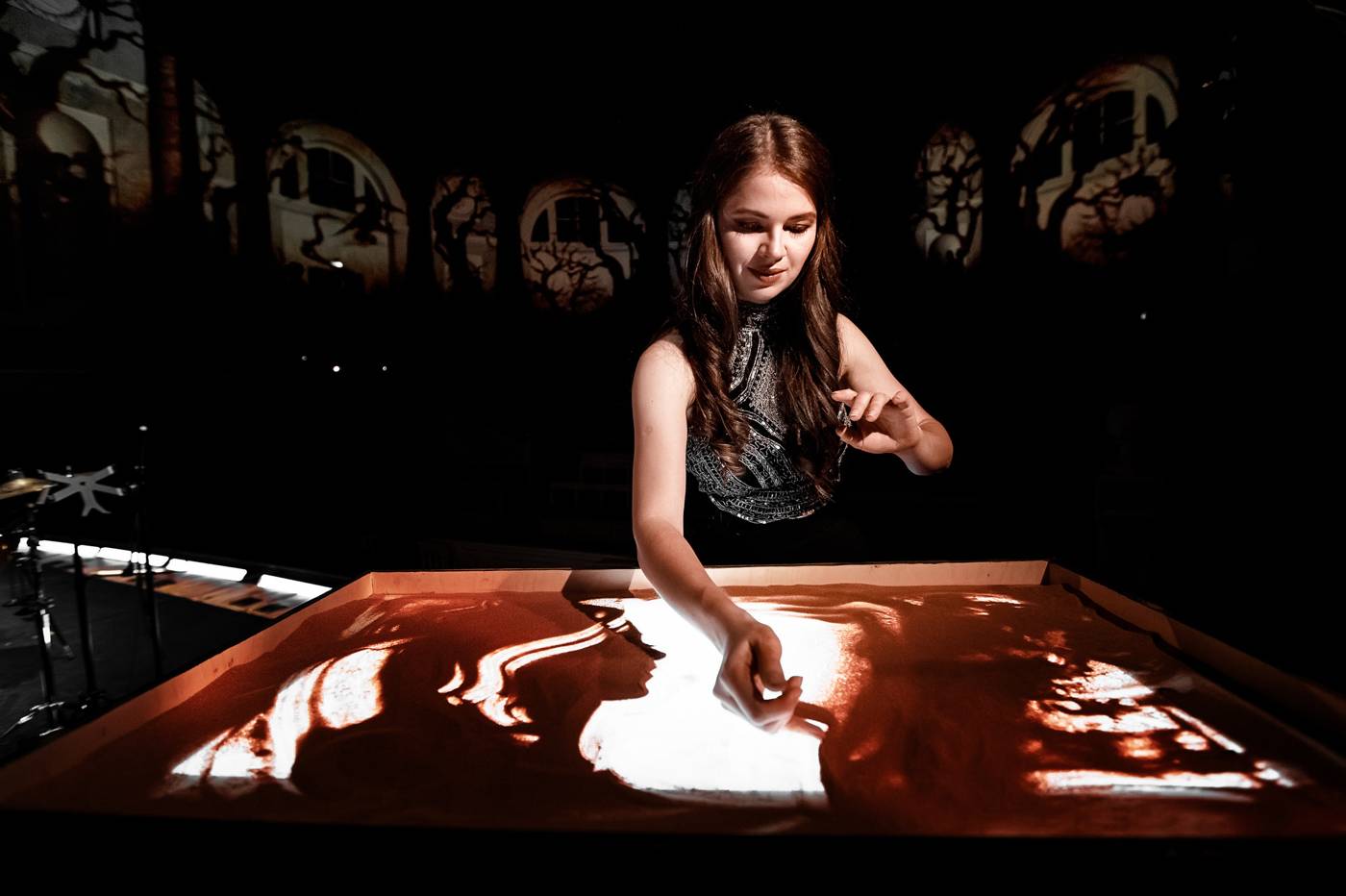 Artista dibujando con arena sobre una mesa de luz frente al público